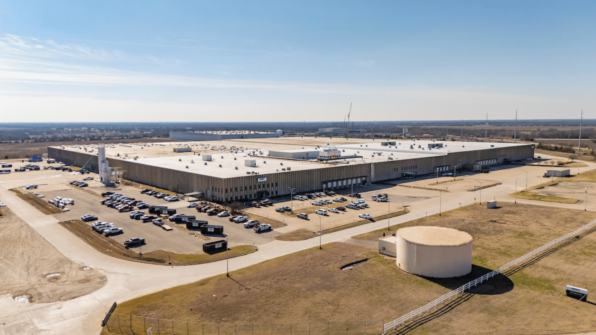 Aerial view of ORBIS Corporation's new manufacturing plant in Greenville, Texas, showcasing a large industrial warehouse complex with ample parking spaces and vehicles, surrounded by open land.